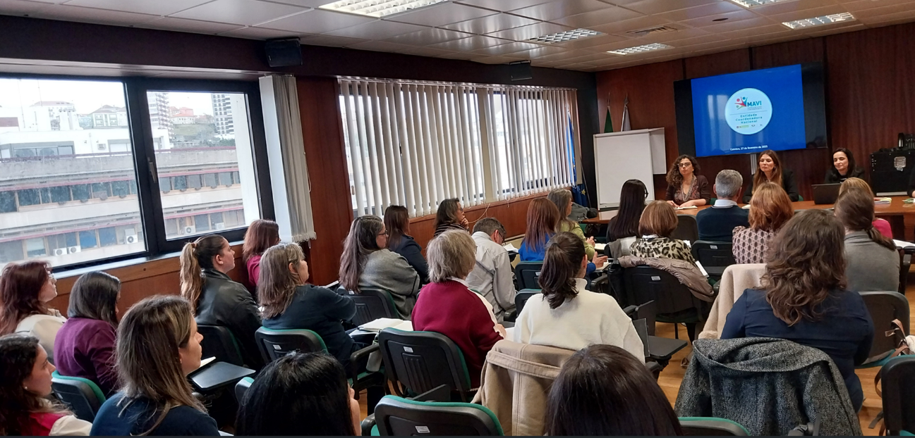 É visível um auditório com público a olhar para três oradoras. Por detrás delas, está uma tela com uma projeção.