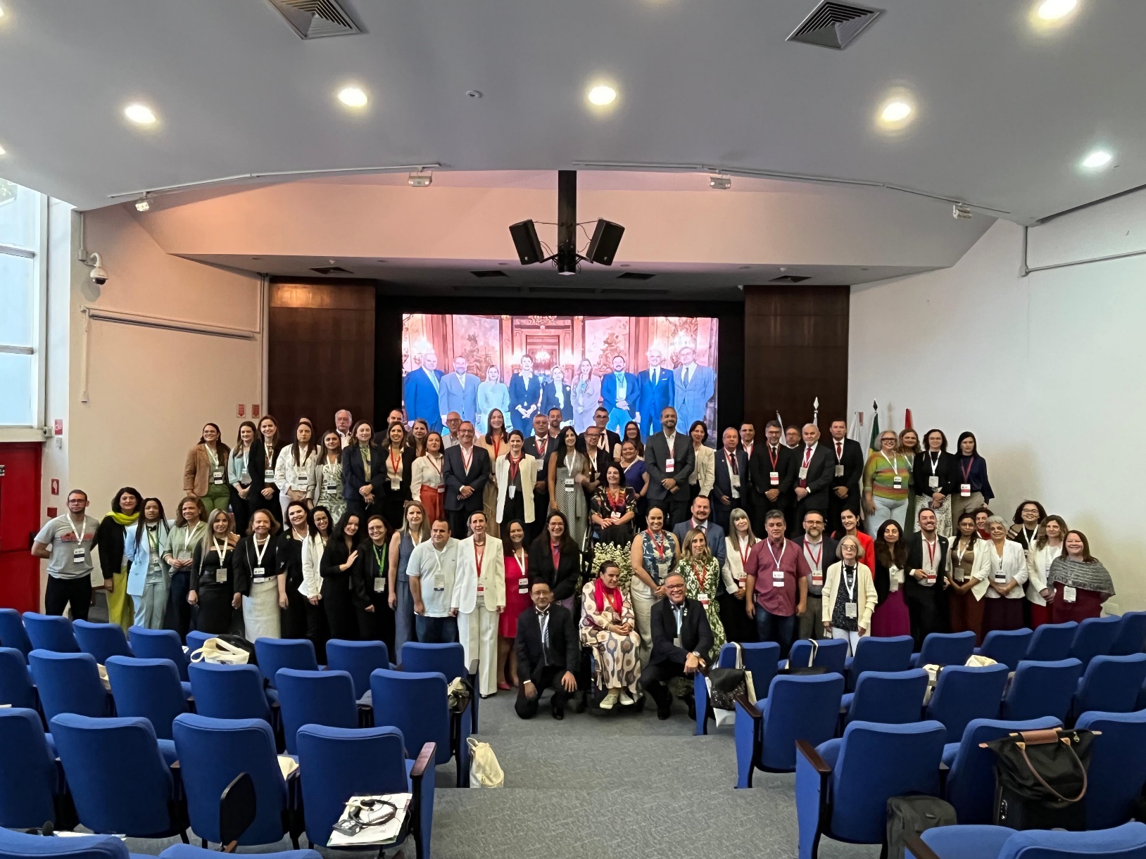  Foto coletiva com todos os participantes dispostos em grupo junto ao palco deste auditório. Collective photo with all participants arranged in a group next to the stage of this auditorium. 