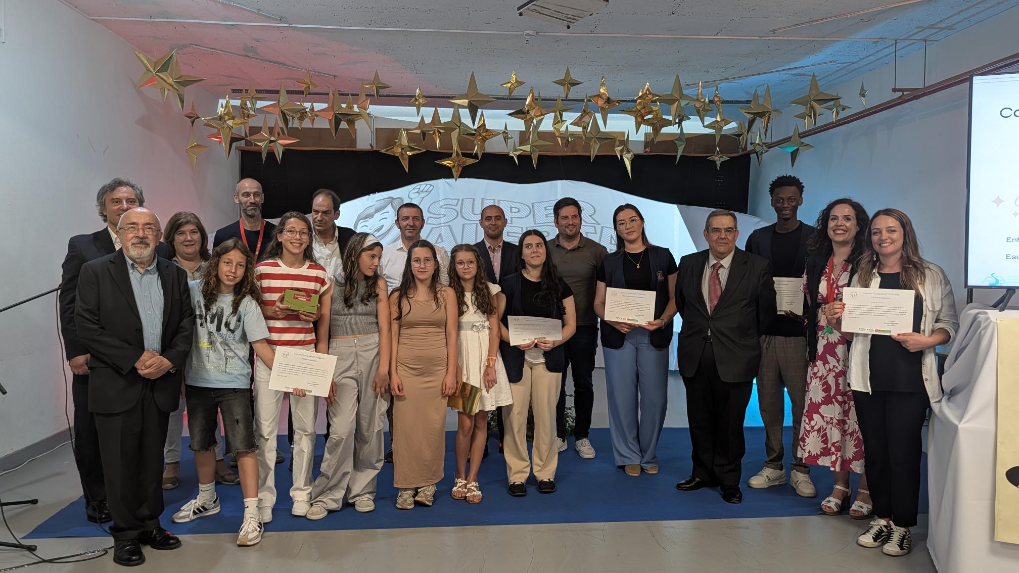Grupo de pessoas alinhadas em palco durante uma cerimónia, algumas estão a segurar certificados. O cenário inclui uma estrutura com fundo onde se lê parcialmente “SUPER ALERTA”. No teto, estão suspensas várias estrelas douradas.