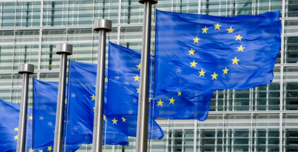 Edifício em aço e e vidro da União Europeia com 5 bandeiras da UE, ao vento.