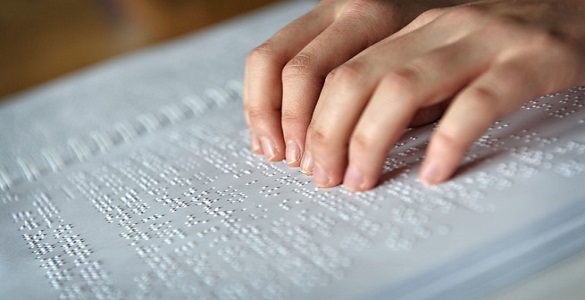 Two Hands on a Book Written in Braille
