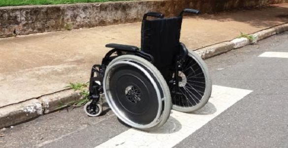 Cadeira de rodas em cima de uma passadeira para peões em frente a um passeio sem rebaixamento.