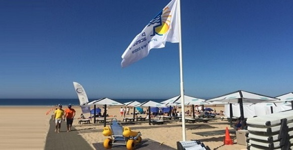 Praia com uma passadeira até ao mar, bandeira “Praia Acessível” hasteada e uma cadeira anfíbia
