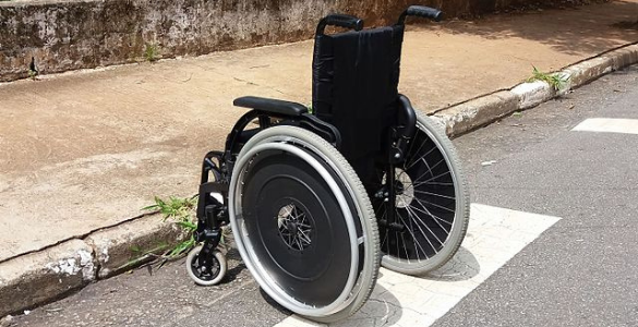 Cadeira de rodas em cima de uma passadeira para peões em frente a um passeio sem rebaixamento