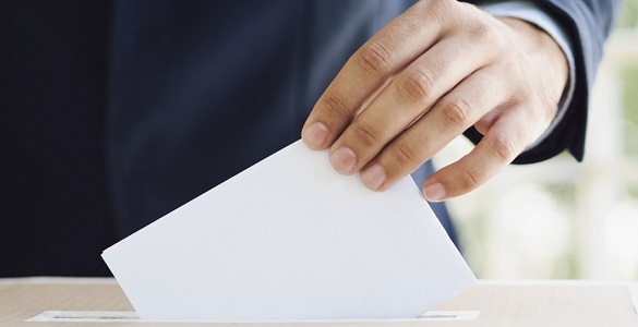 Mão a colocar um boletim de voto na ranhura de uma urna.