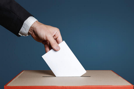 A imagem mostra uma mão a inserir um boletim de voto numa urna.